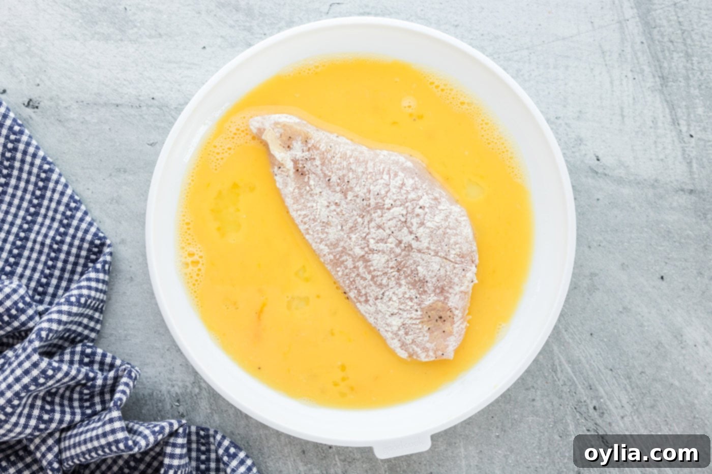 four dredged chicken breasts in egg mixture