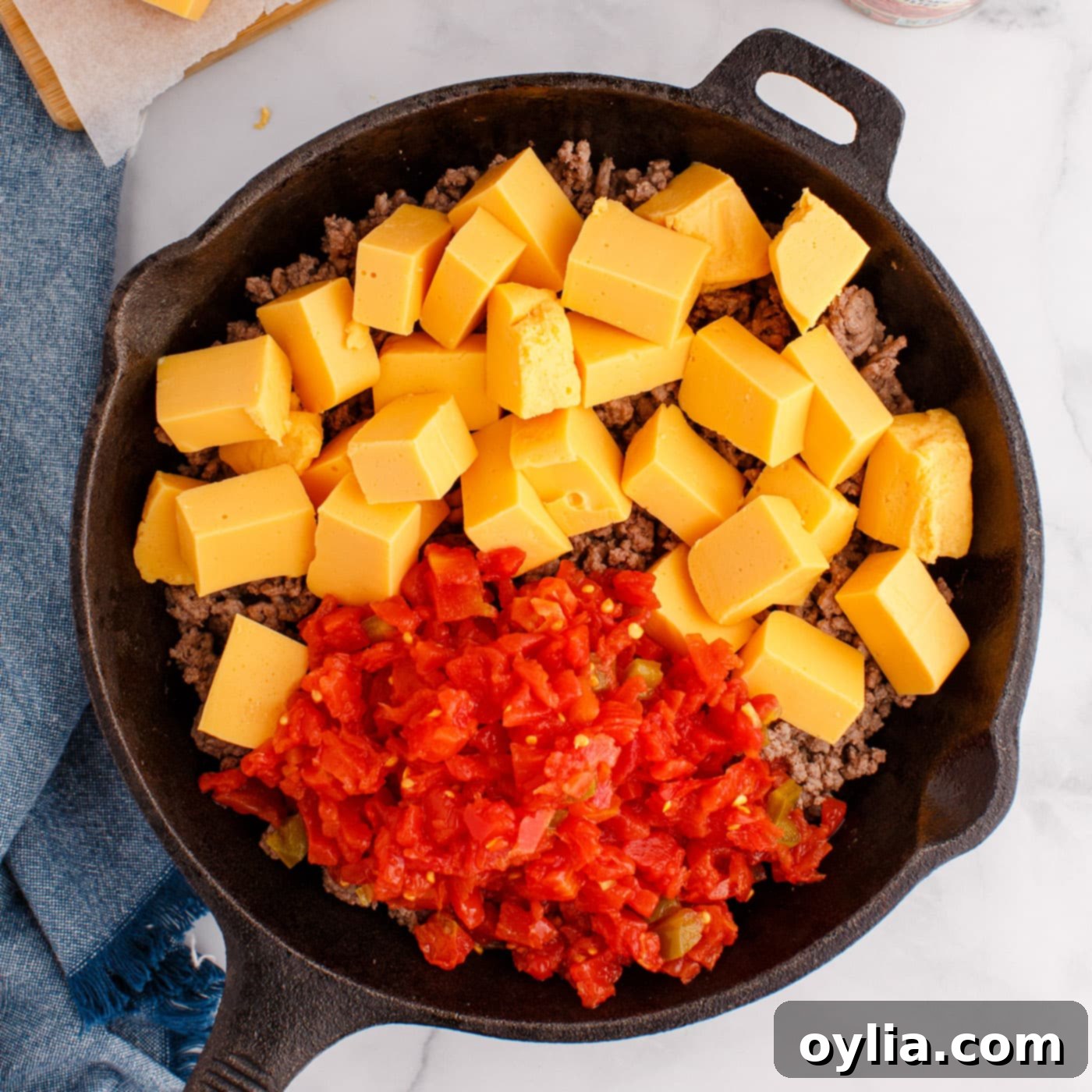 Rotel tomatoes, Velveeta cheese cubes, and ground beef simmering together in a skillet, melting into a dip