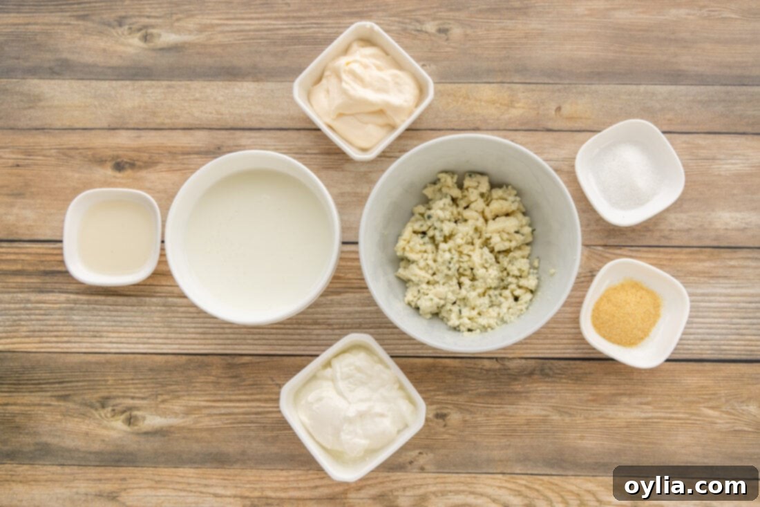 A collection of fresh ingredients laid out for making blue cheese dressing: buttermilk, blue cheese crumbles, mayonnaise, sour cream, garlic powder, sugar, and white wine vinegar.