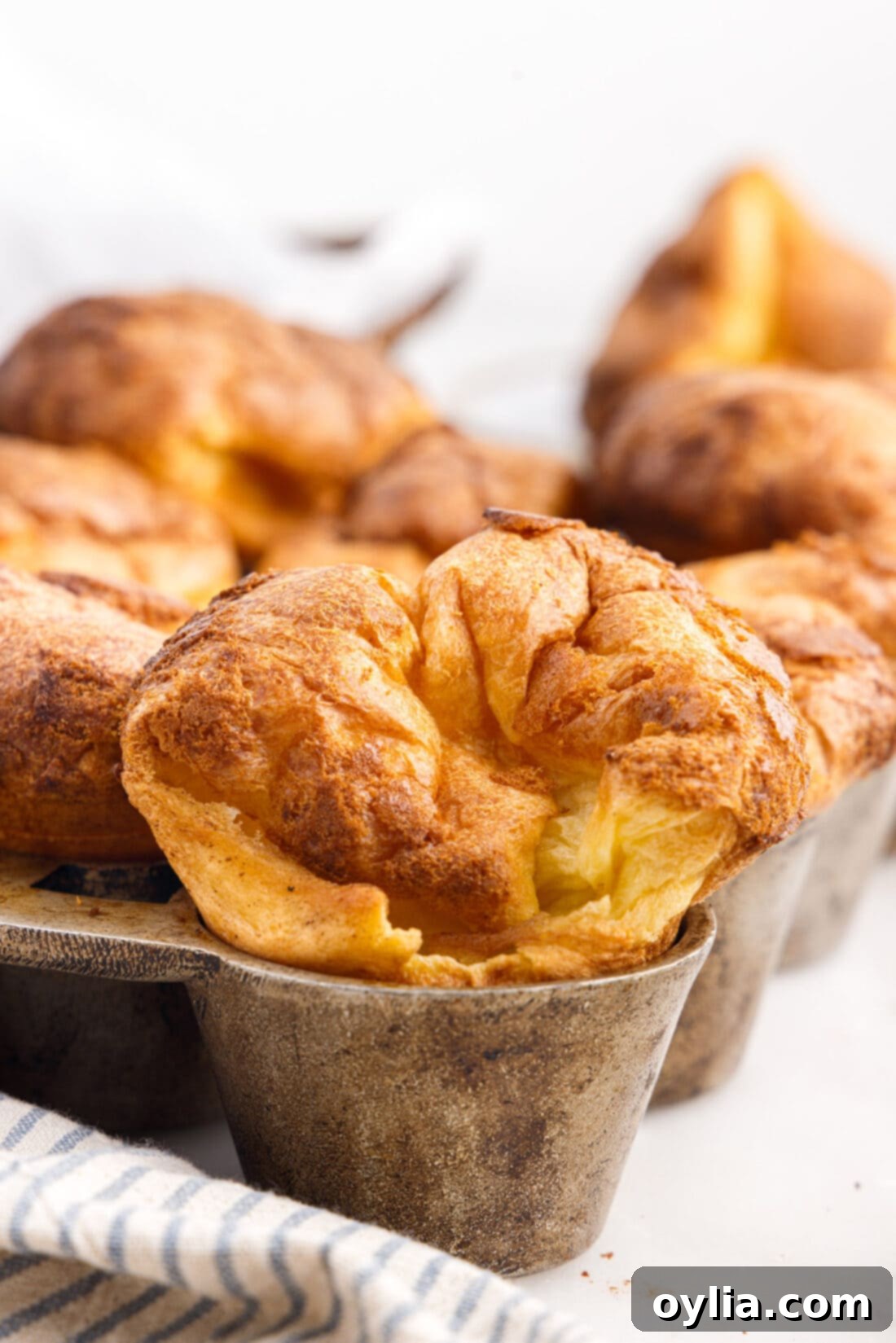 Freshly baked golden popovers in a specialized popover pan, showcasing their tall, puffed shape.
