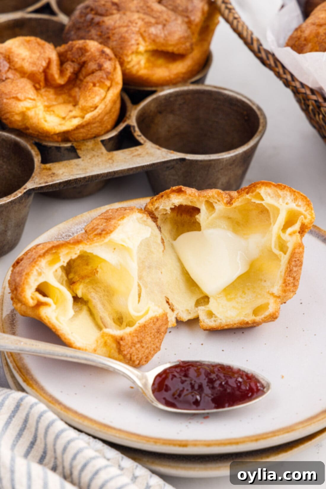 A freshly baked popover, torn open, with a generous spread of butter and jam, ready to be eaten.