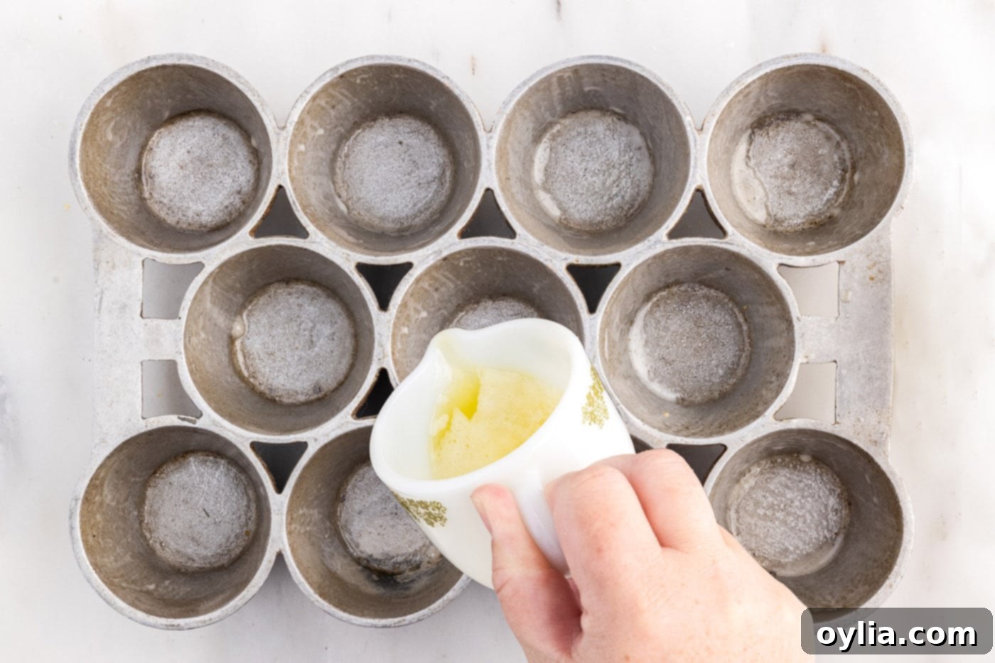 Pouring melted butter into the individual wells of a preheated popover pan, which is hot.