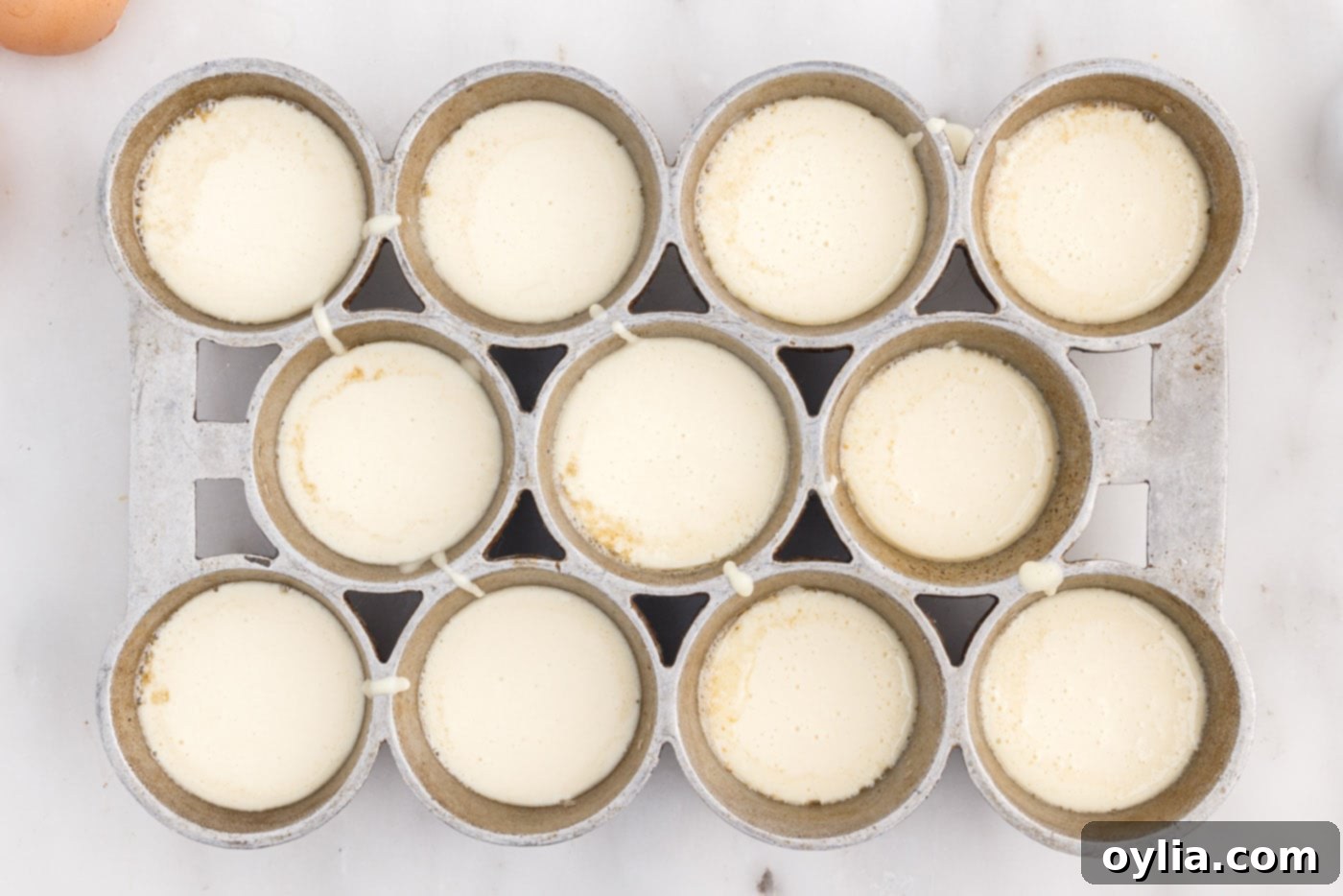 Popover batter evenly distributed in the popover tin cups, ready for baking.