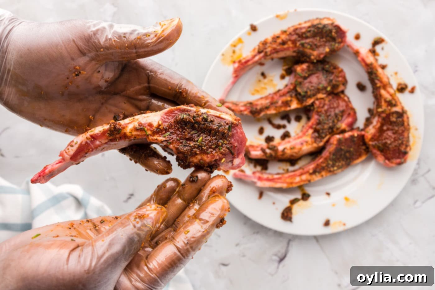 Hands rubbing lamb chops with a spice and oil mixture