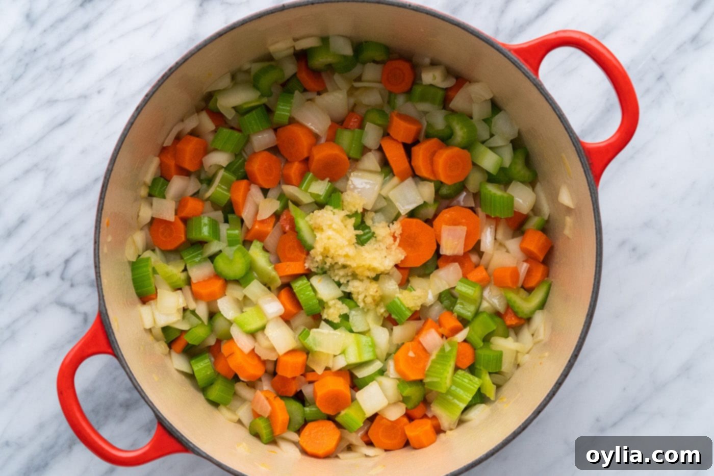 adding minced garlic to onion, celery, and carrots in a pot
