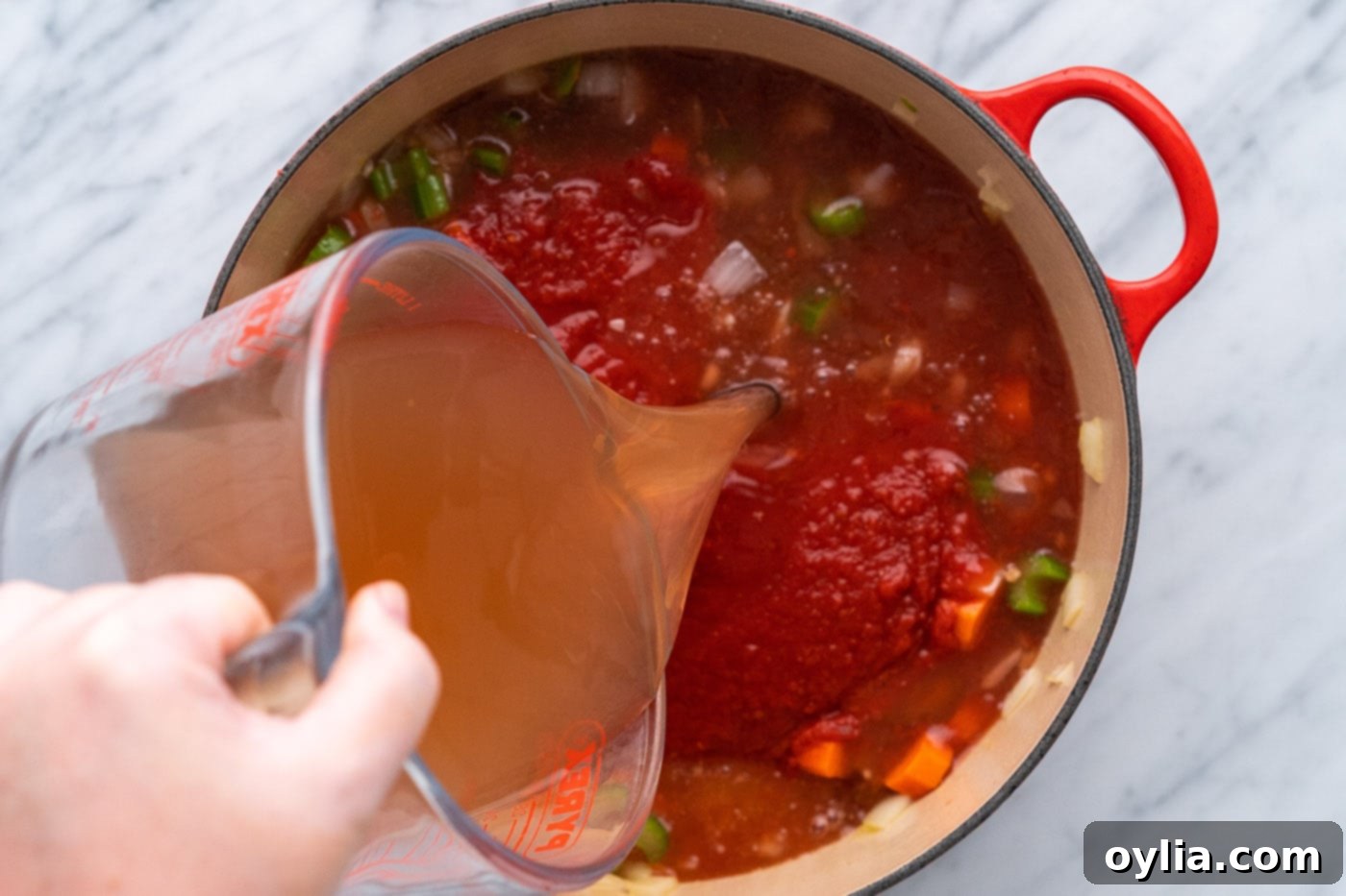 pouring vegetable broth over diced tomatoes, celery, onion, and carrot