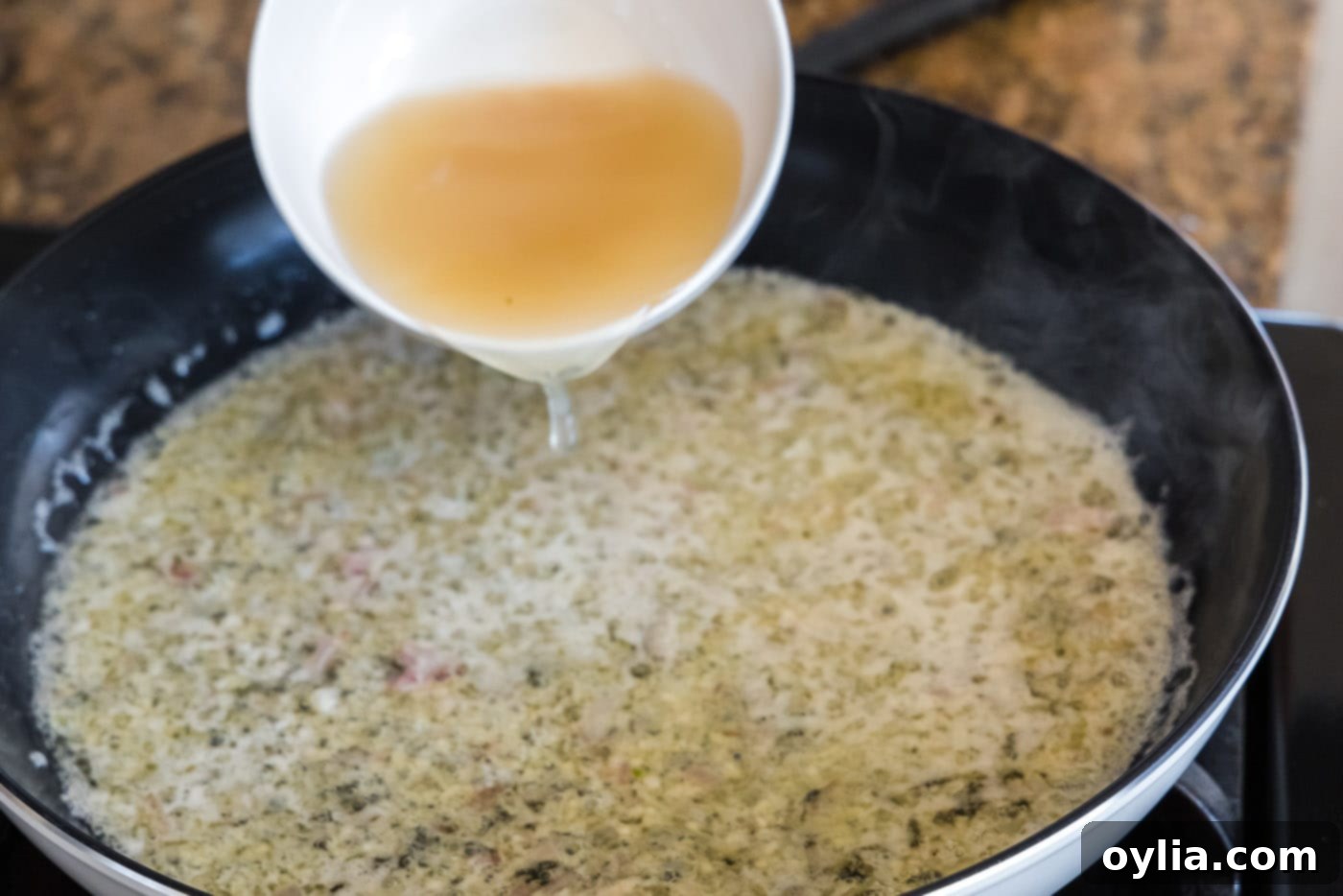 Pouring seafood stock into the simmering thermidor sauce base.