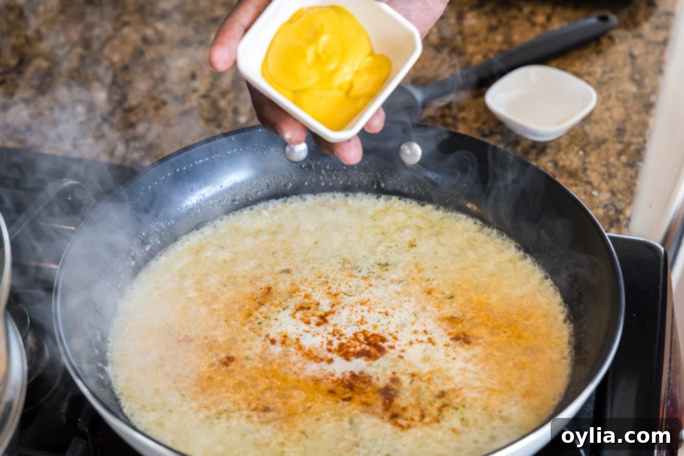 Adding yellow mustard to the lobster thermidor sauce mixture in the skillet.