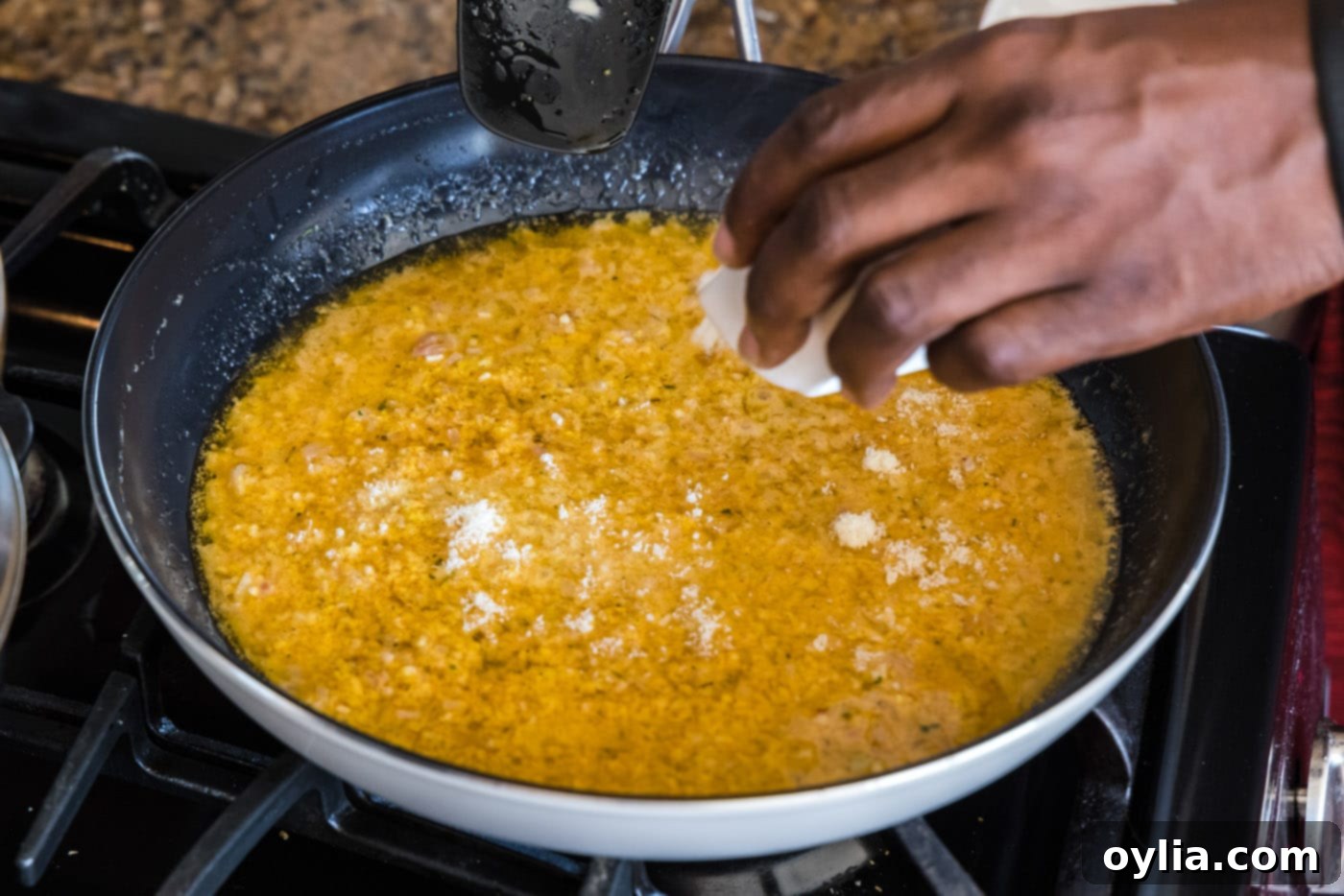 Sprinkling shredded parmesan cheese into the thermidor sauce in a skillet.