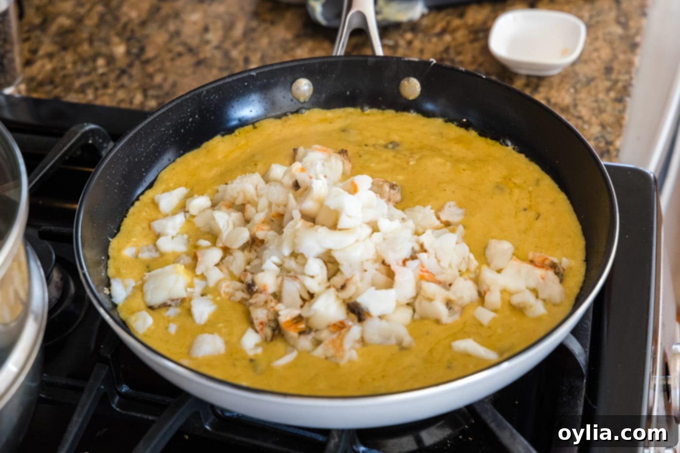 Chopped lobster meat mixed into the creamy thermidor sauce in a skillet.