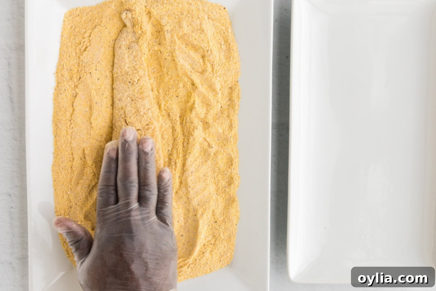 Golden Fried Whiting 7 A hand gently pressing a fish fillet into the cornmeal coating on a baking sheet
