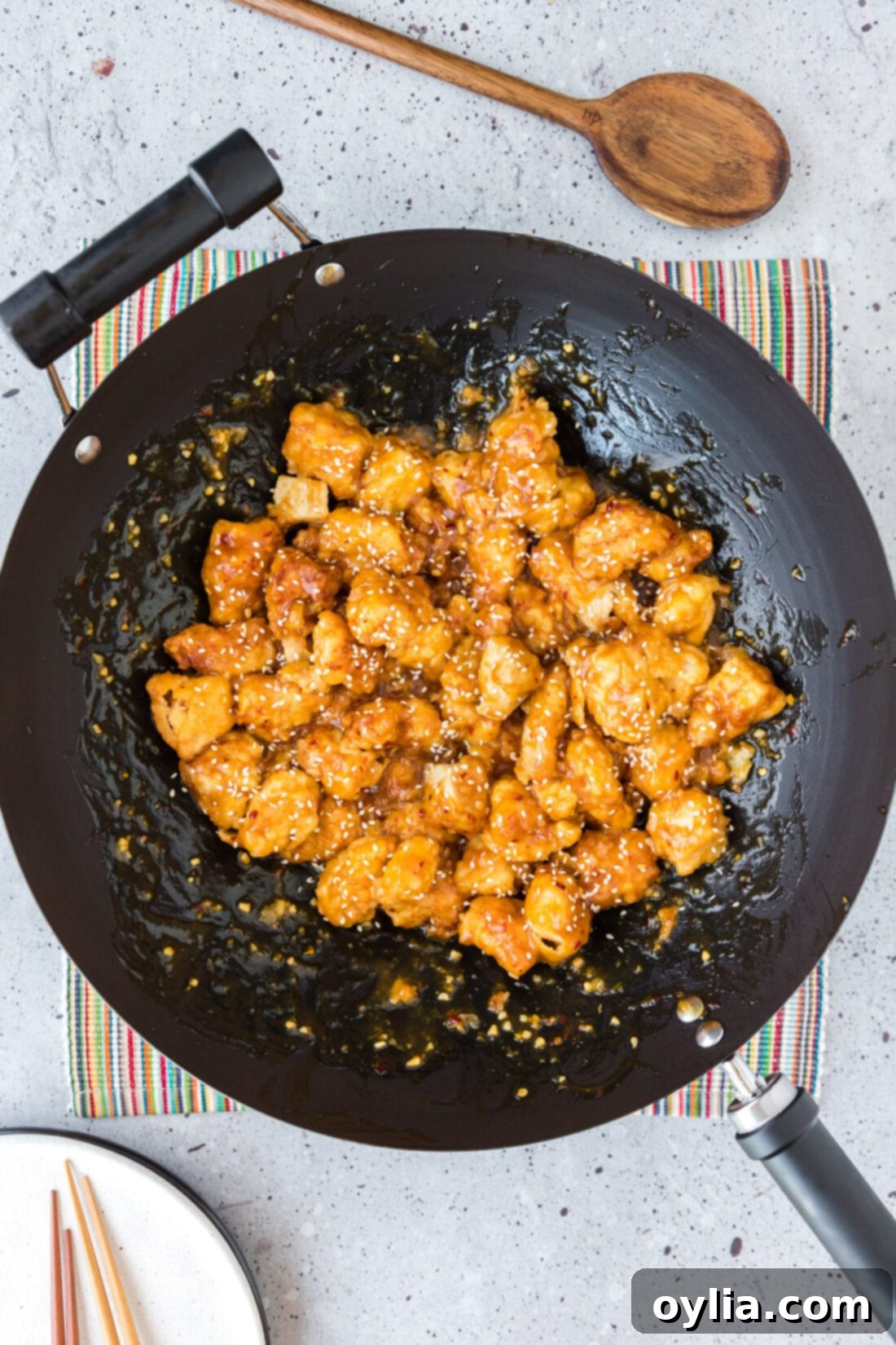 Crispy Orange Chicken in a wok, garnished with sesame seeds