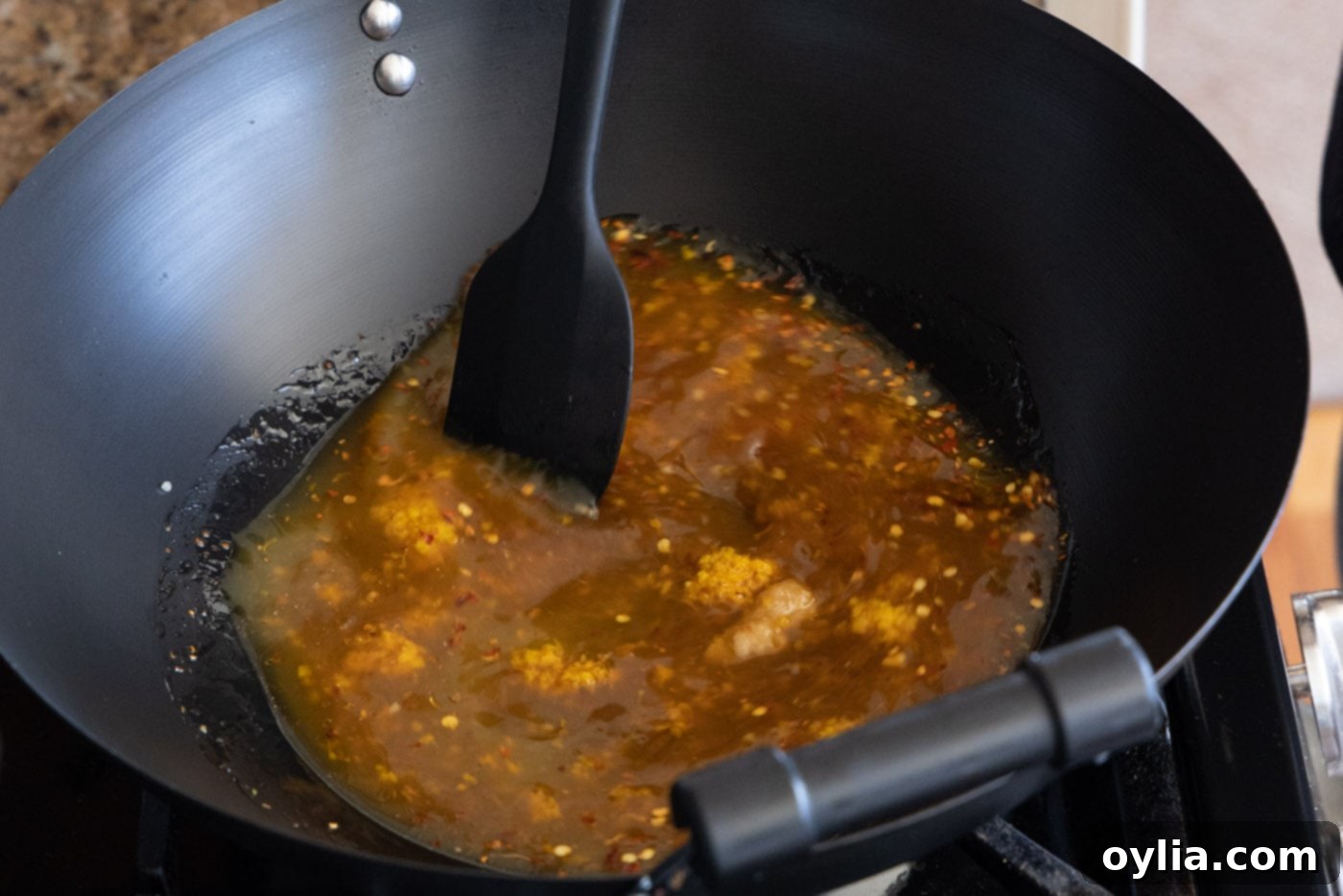 Spatula stirring a bubbling orange chicken sauce mixture in a skillet