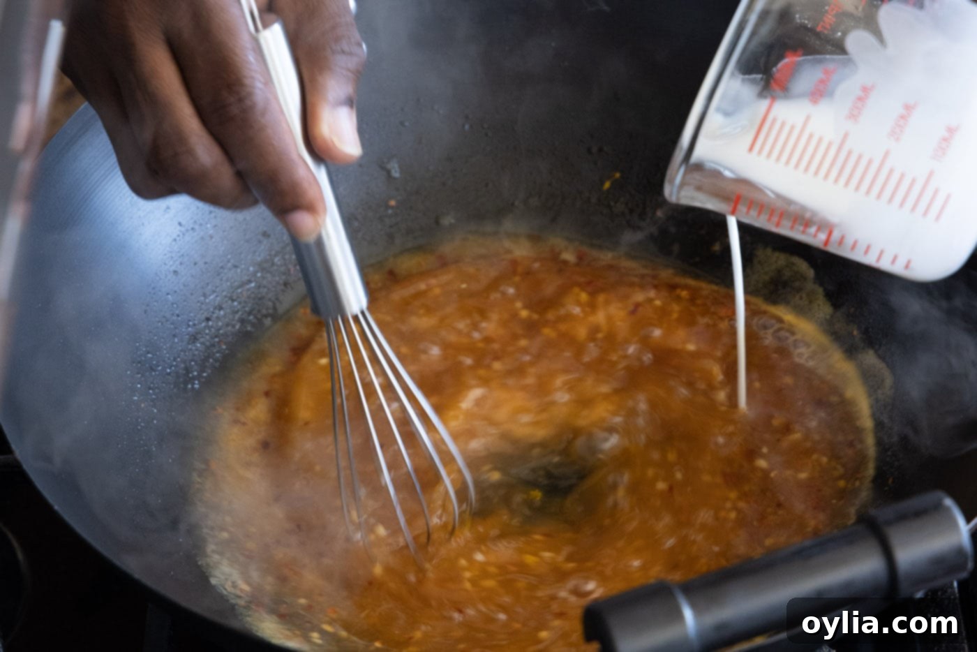 Whisk incorporating cornstarch slurry into the orange sauce in a skillet