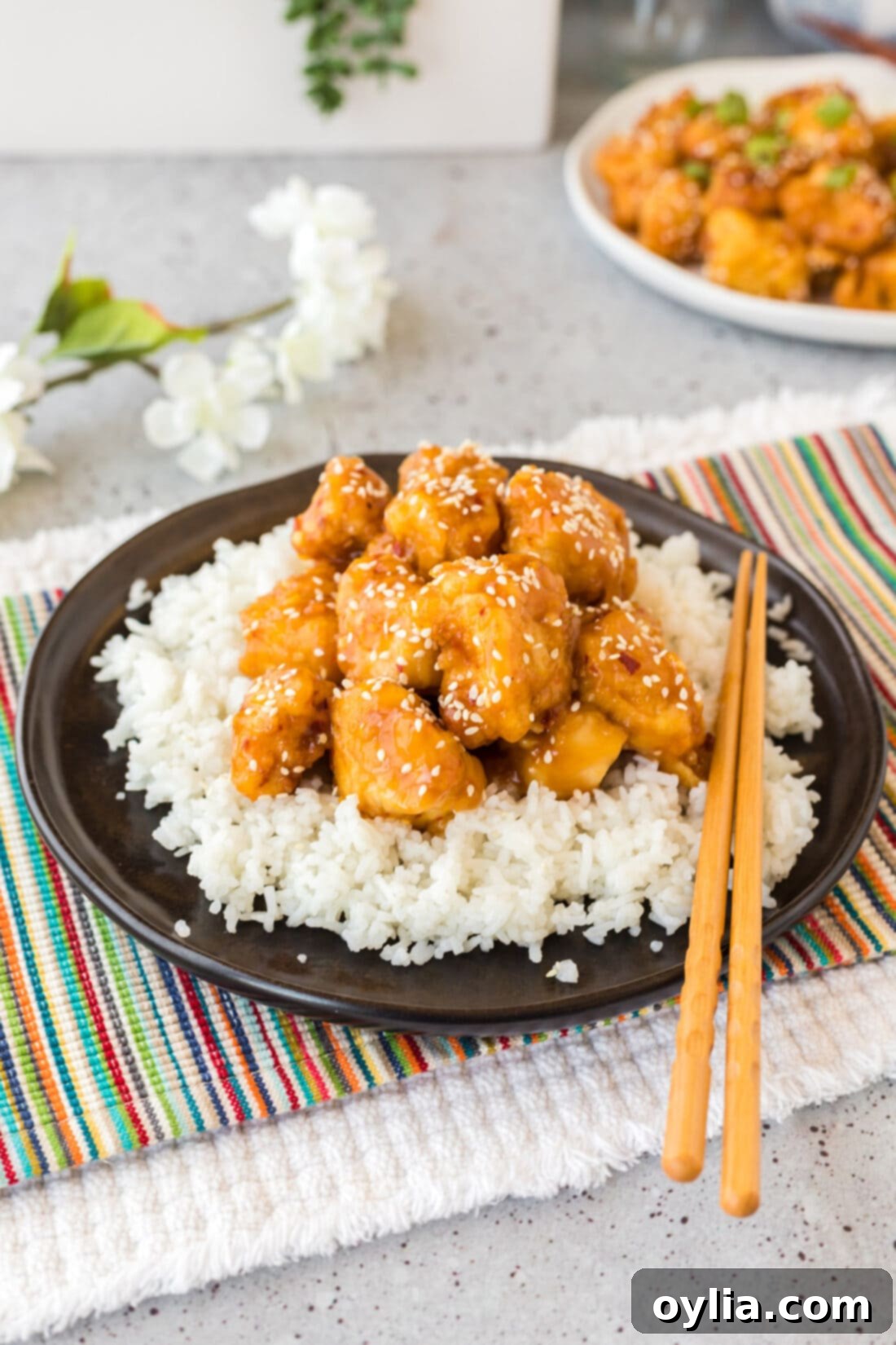 A beautifully plated dish of crispy homemade orange chicken served over white rice, garnished with green onions and sesame seeds.
