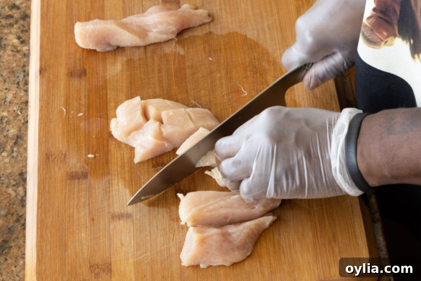 Chef knife chopping boneless chicken breasts into uniform pieces for orange chicken