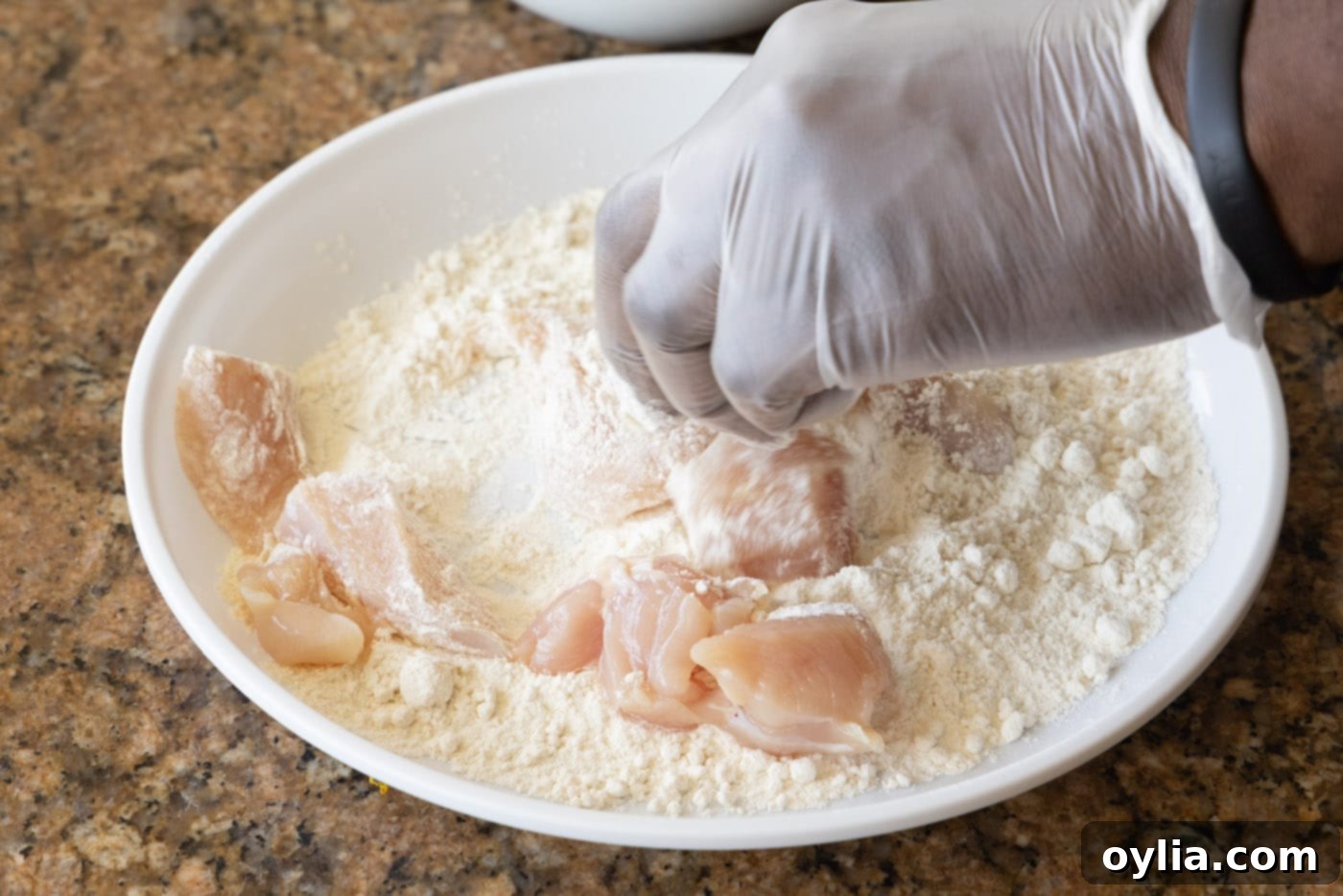 Hand dredging chicken pieces in a bowl of flour for frying