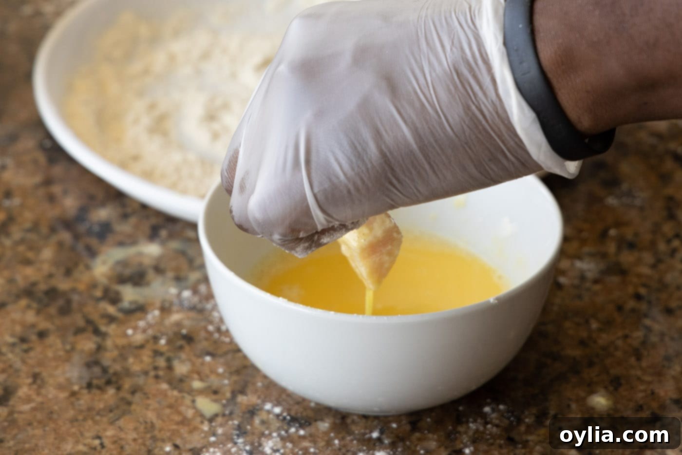 Chicken pieces being dipped into whisked egg in a white dish