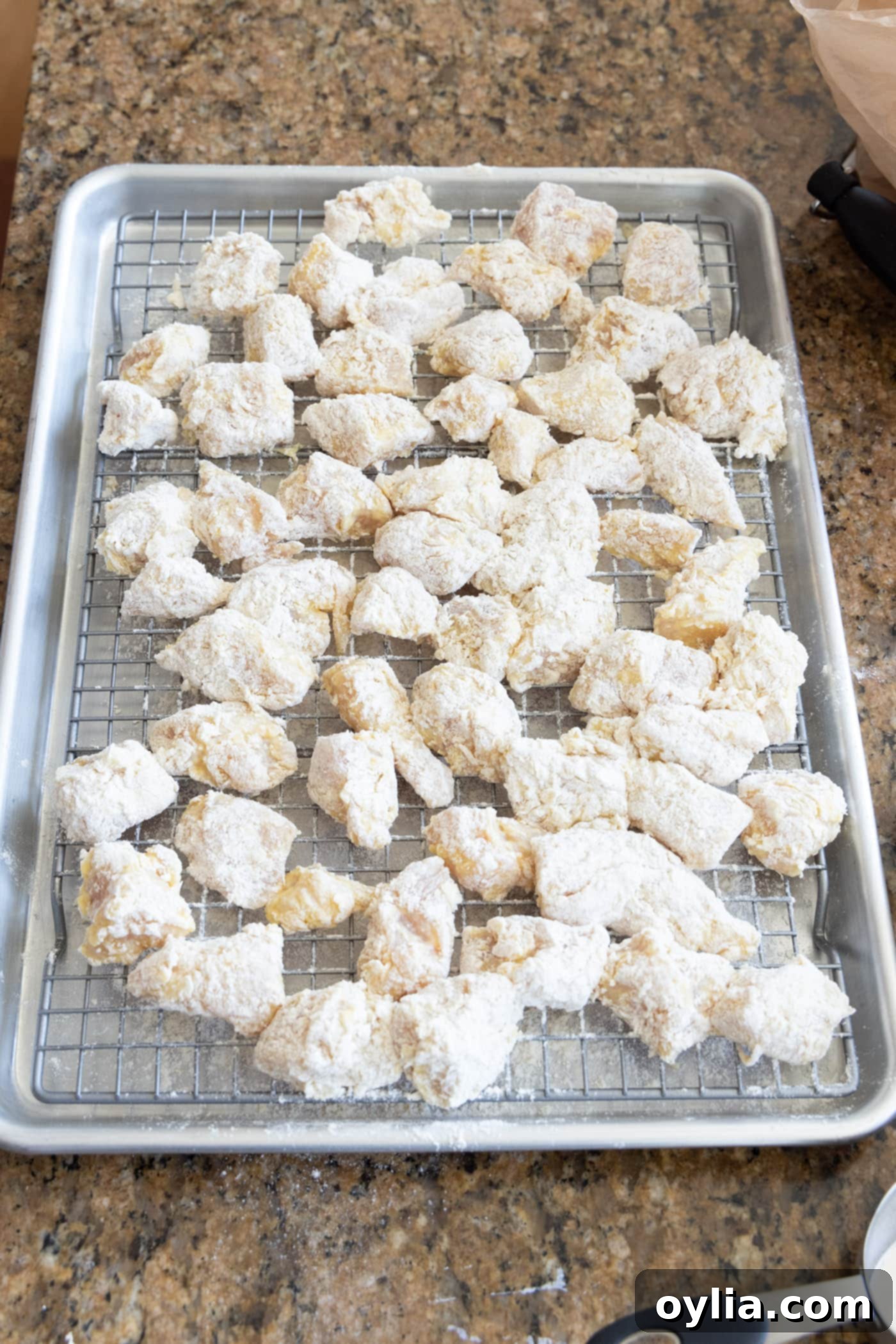 Dredged chicken pieces resting on a wire rack before frying