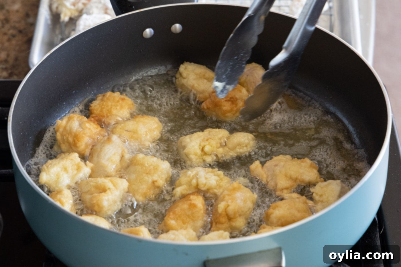 A hand flipping pieces of chicken in a hot skillet with oil