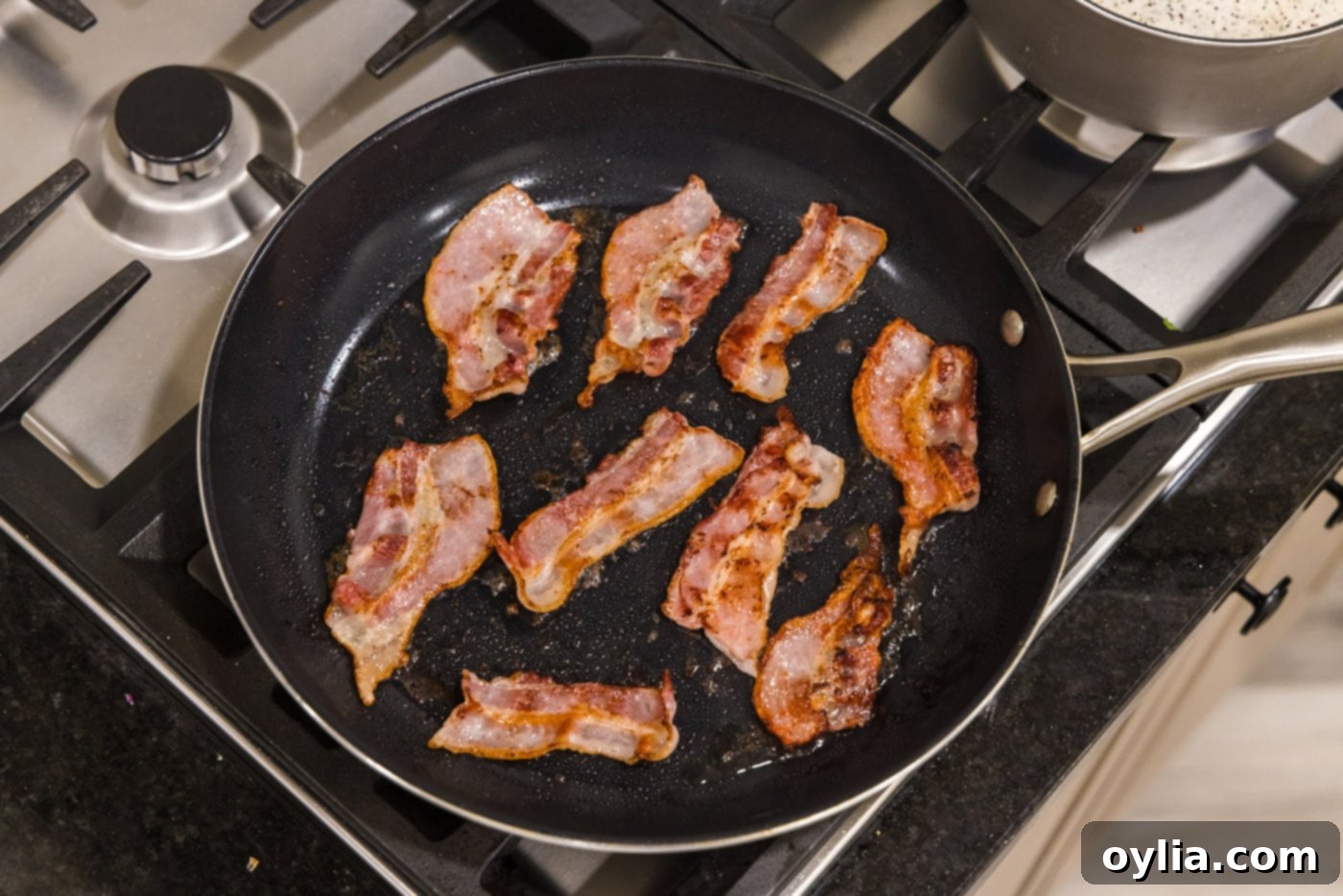 Bacon cooking and crisping up in a hot skillet, rendering its fat.