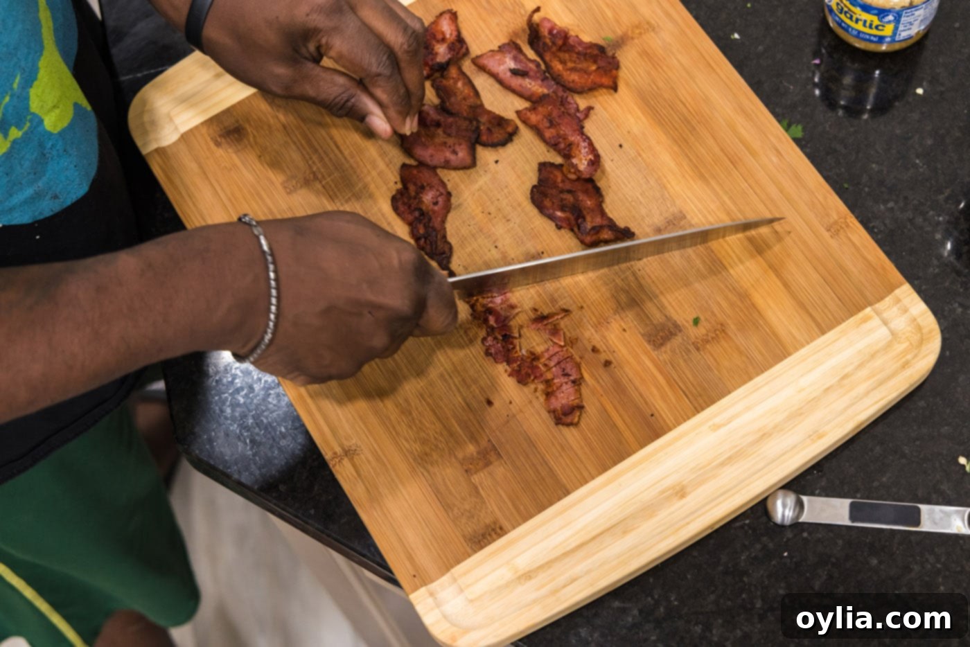 Chopping crispy bacon into small bits on a cutting board.