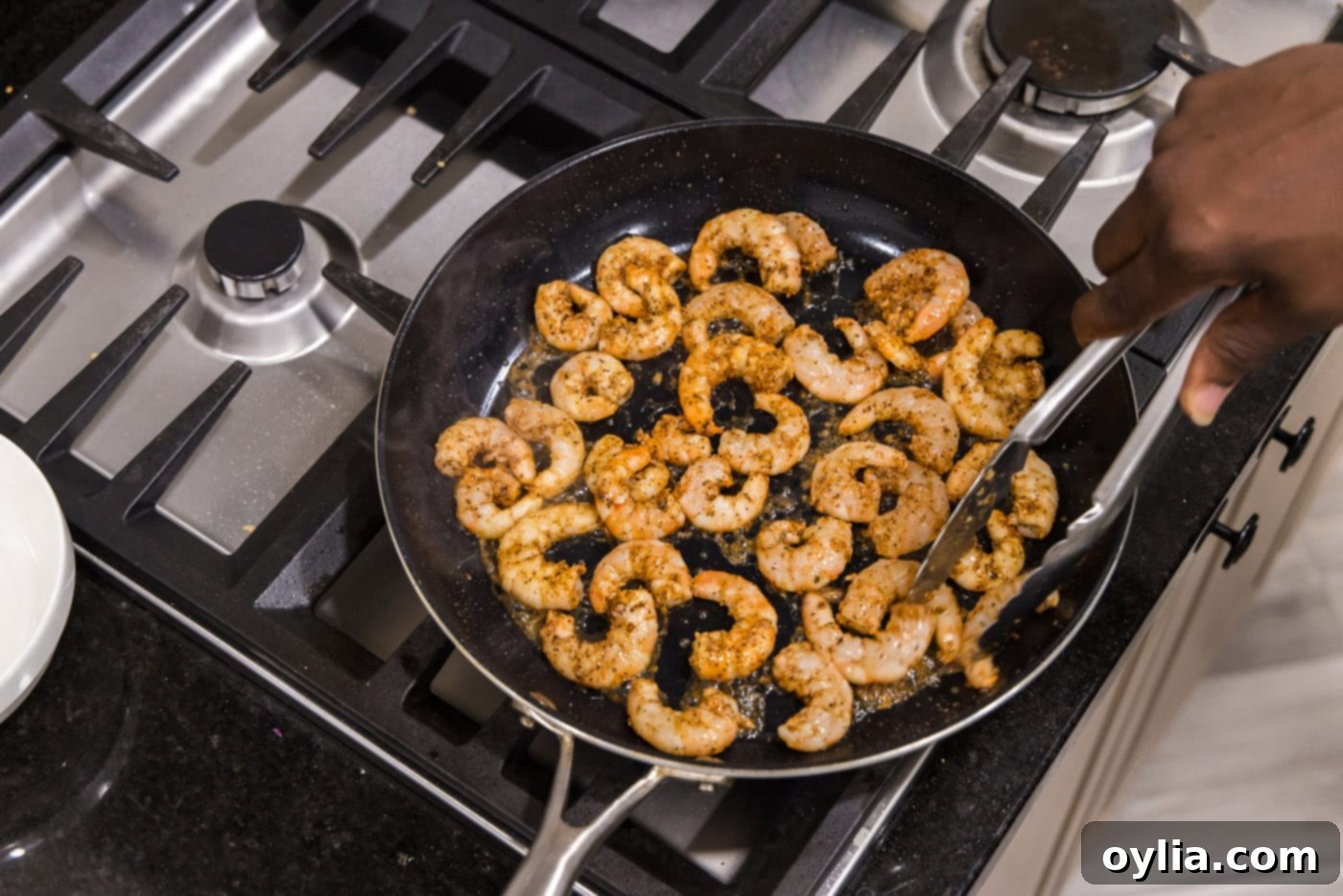Cajun seasoned shrimp cooking in bacon grease with minced garlic in a skillet.