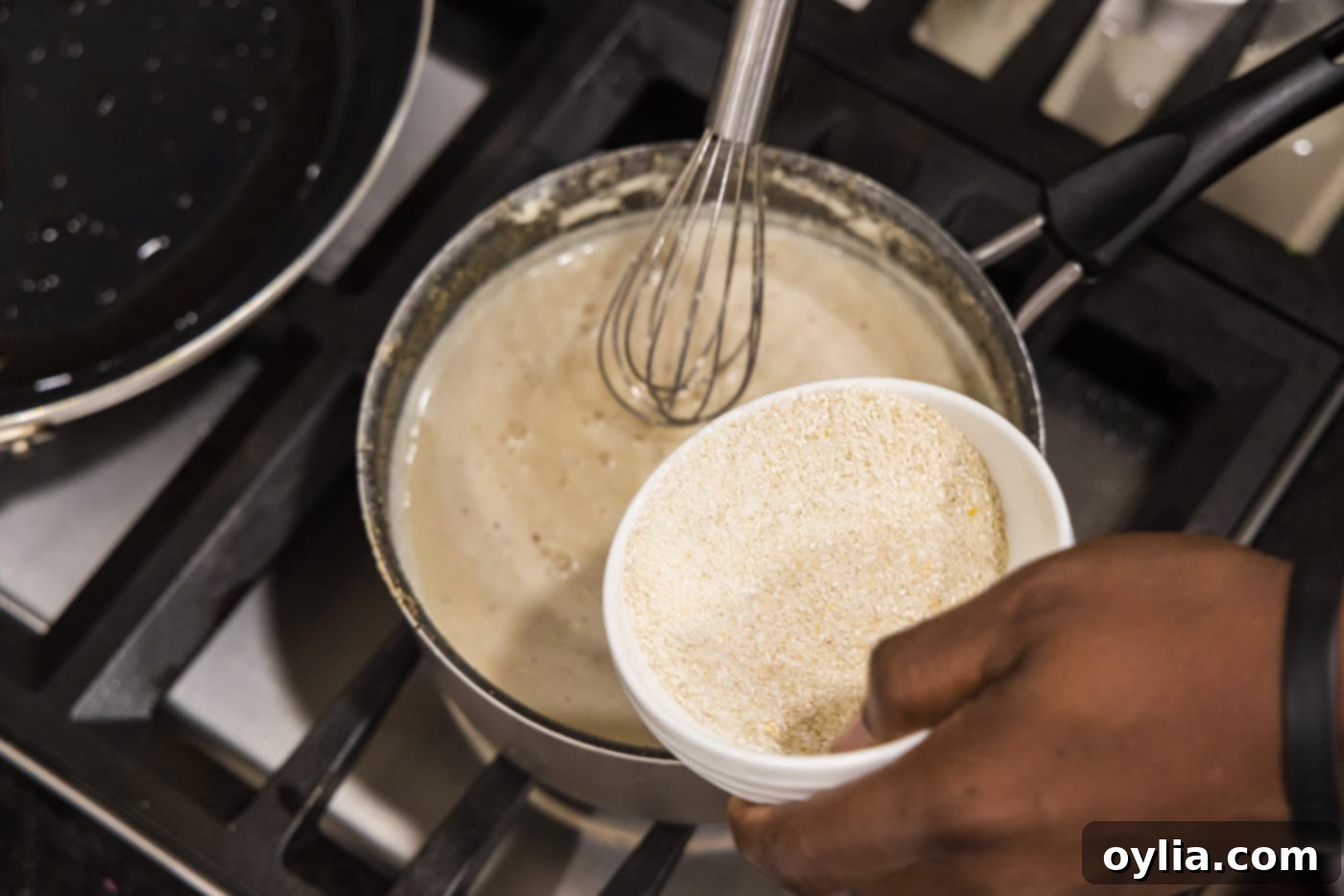 Whisking grits into the boiling liquid in a saucepan to prevent lumps.