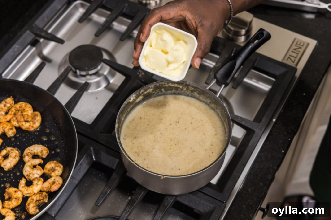 Adding butter to the cooked grits in a saucepan.