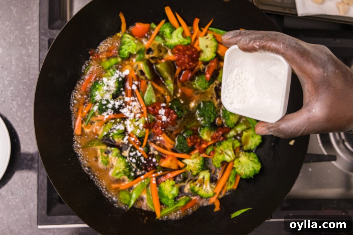 sprinkling cornstarch over veggies in a wok