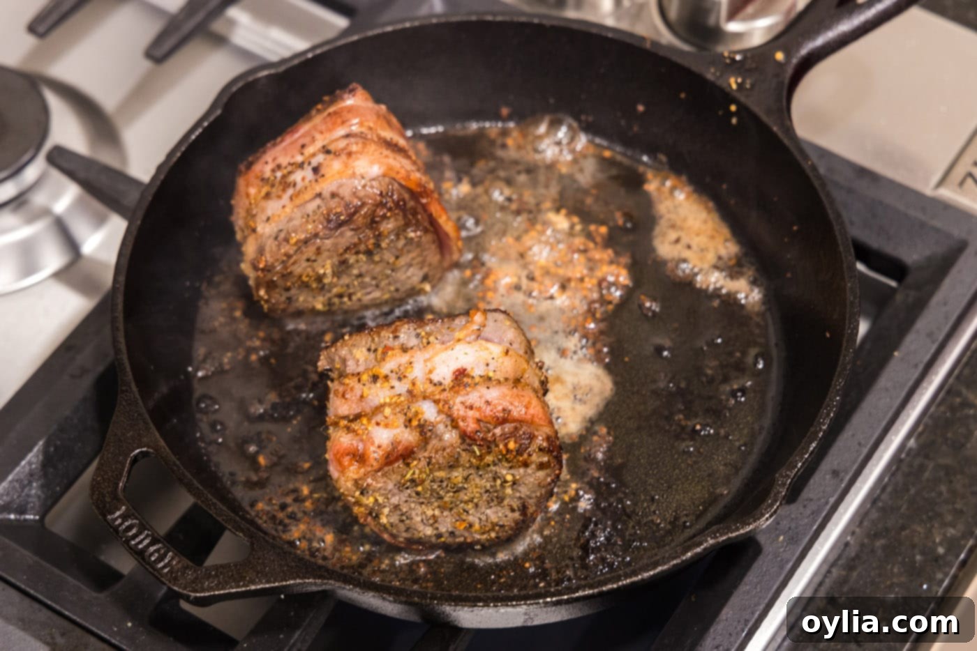 Close-up of a bacon wrapped filet mignon searing, showing a crispy bacon and browned crust.