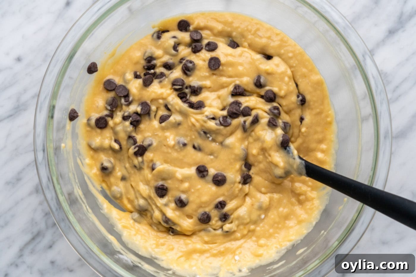 Mixing chocolate chips into the muffin batter with a spatula.