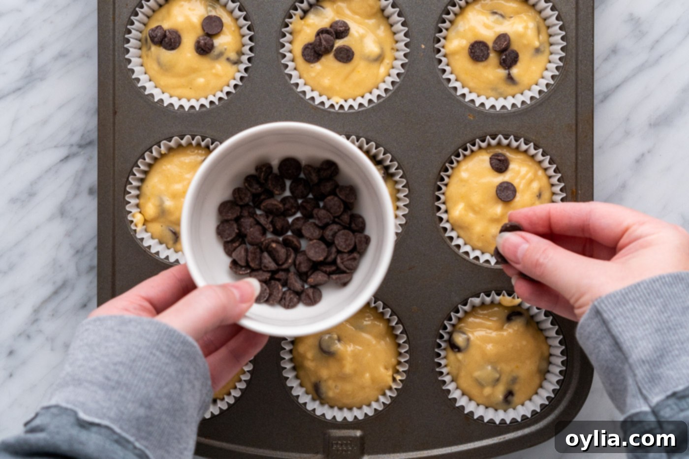 Adding extra chocolate chips on top of muffin batter in a pan for an appealing finish.