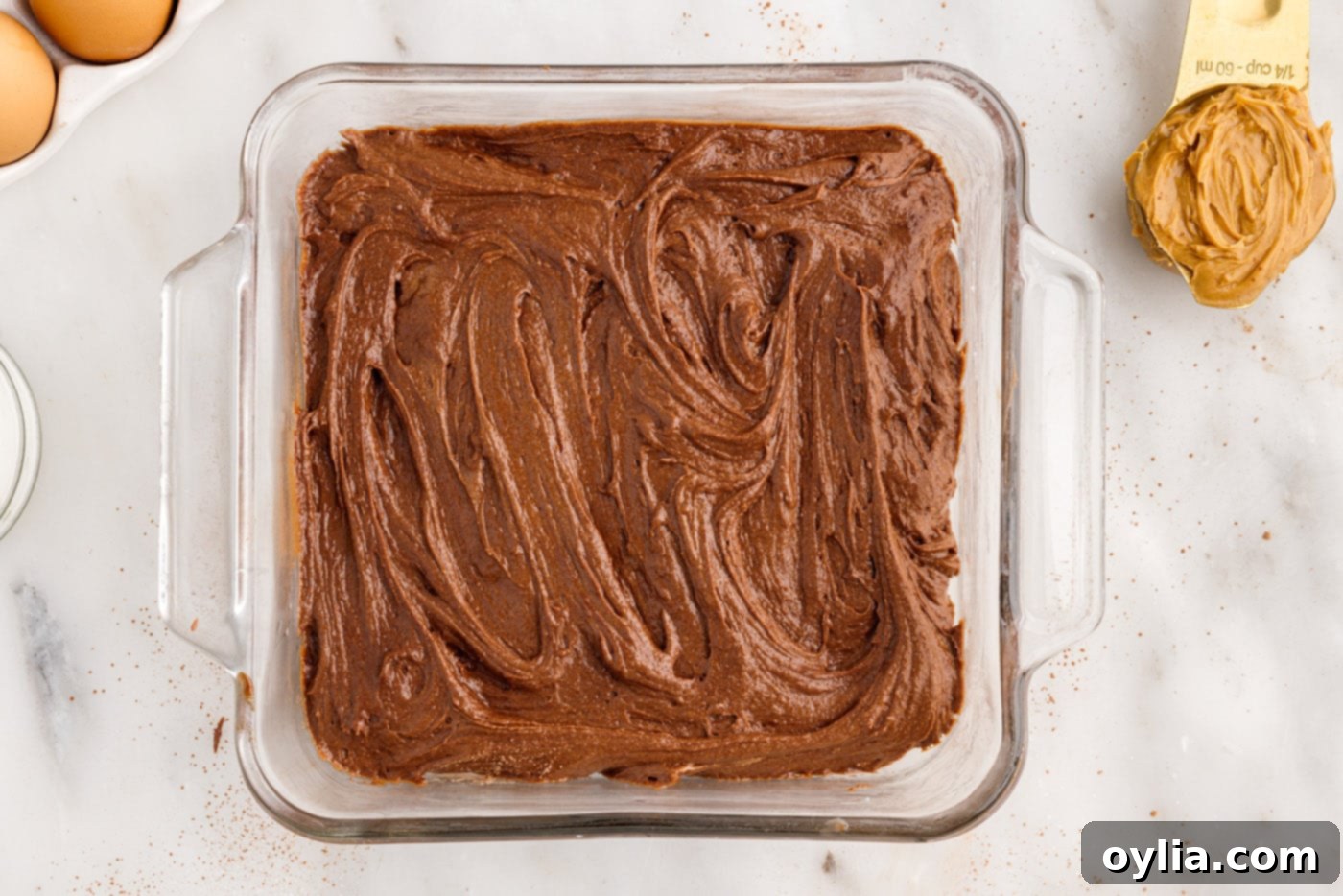 Evenly spread chocolate brownie batter in a square baking dish, ready for the peanut butter swirl.