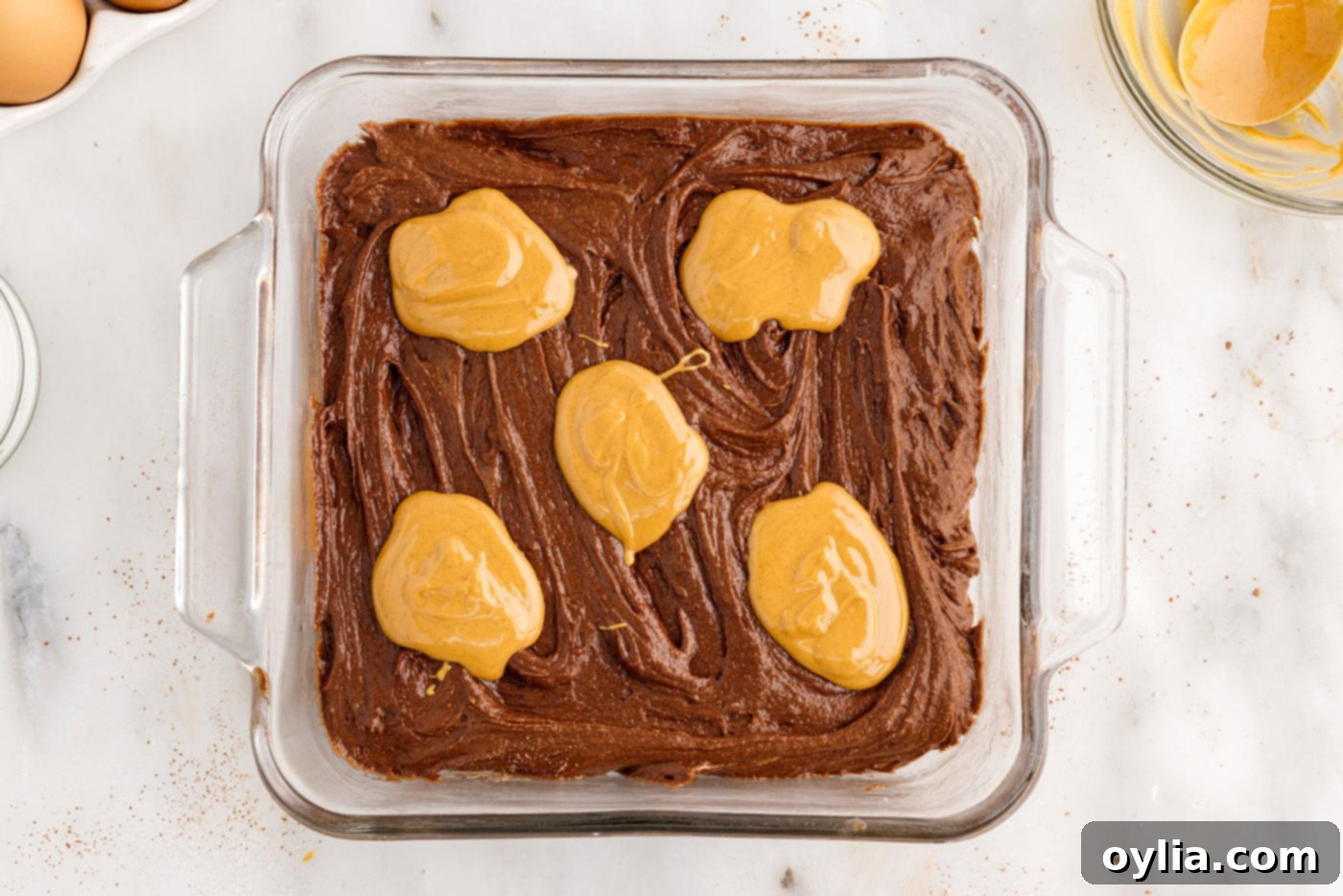 Dollops of melted creamy peanut butter spooned onto the surface of the brownie batter, ready for swirling.