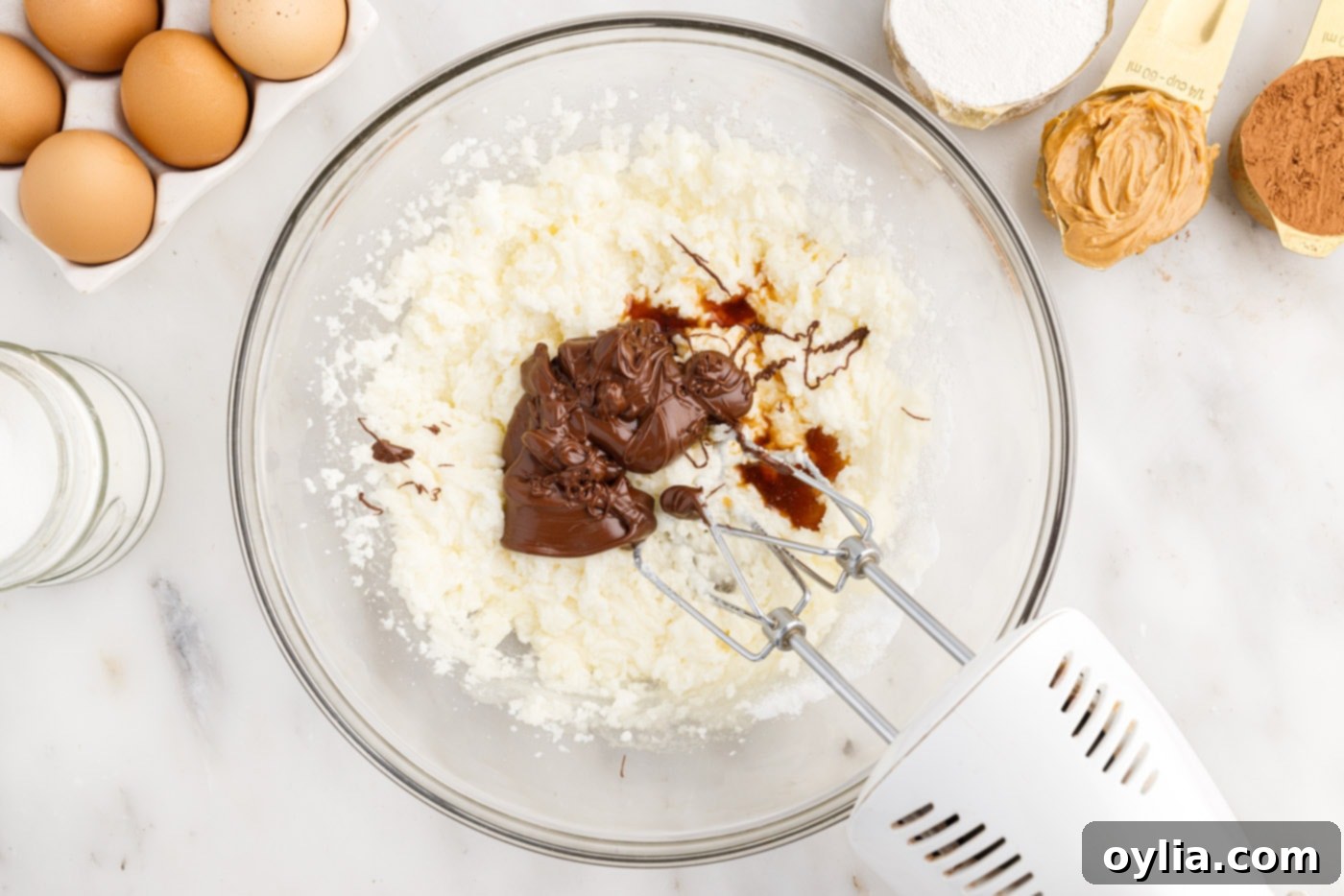 Hand mixer combining melted chocolate and vanilla extract into the butter and sugar mixture for rich brownie batter.