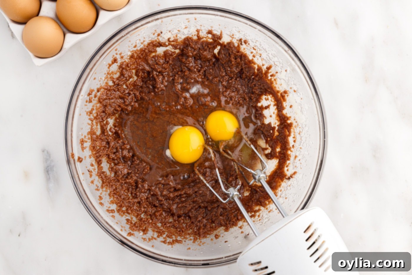 Adding large eggs to the wet brownie batter mixture in a mixing bowl.