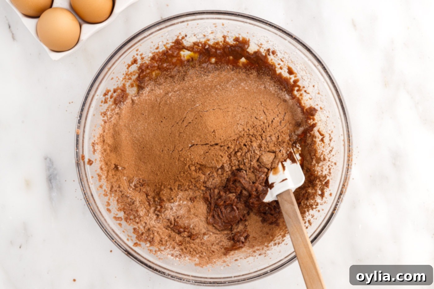 A rubber spatula gently mixing dry ingredients into rich brownie batter.