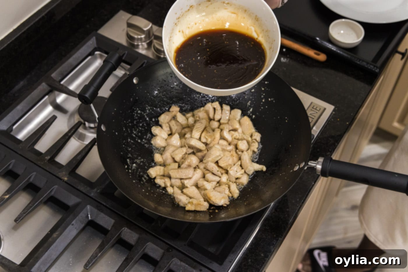 adding teriyaki sauce to wok with cooked chicken