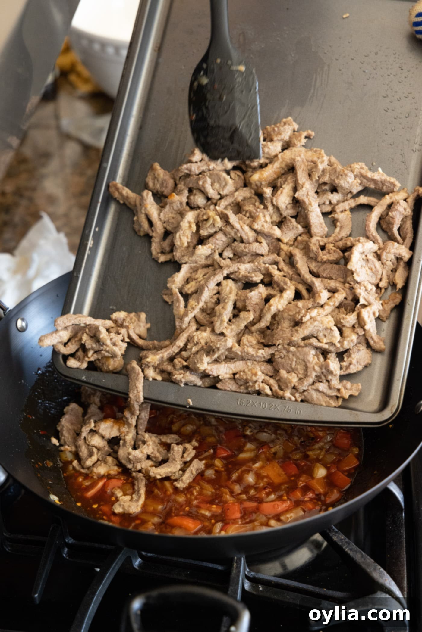 adding cooked beef and vegetables to skillet with sauce