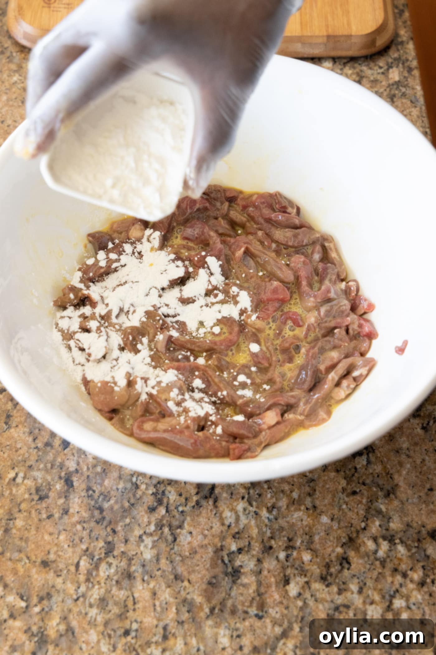 adding cornstarch to egg and beef mixture in a bowl, mixing with gloved hands