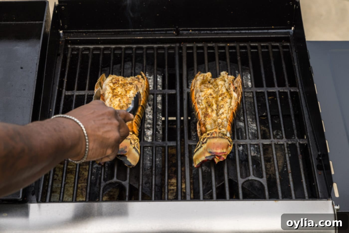 Tongs flipping lobster tails over on the grill to cook the other side