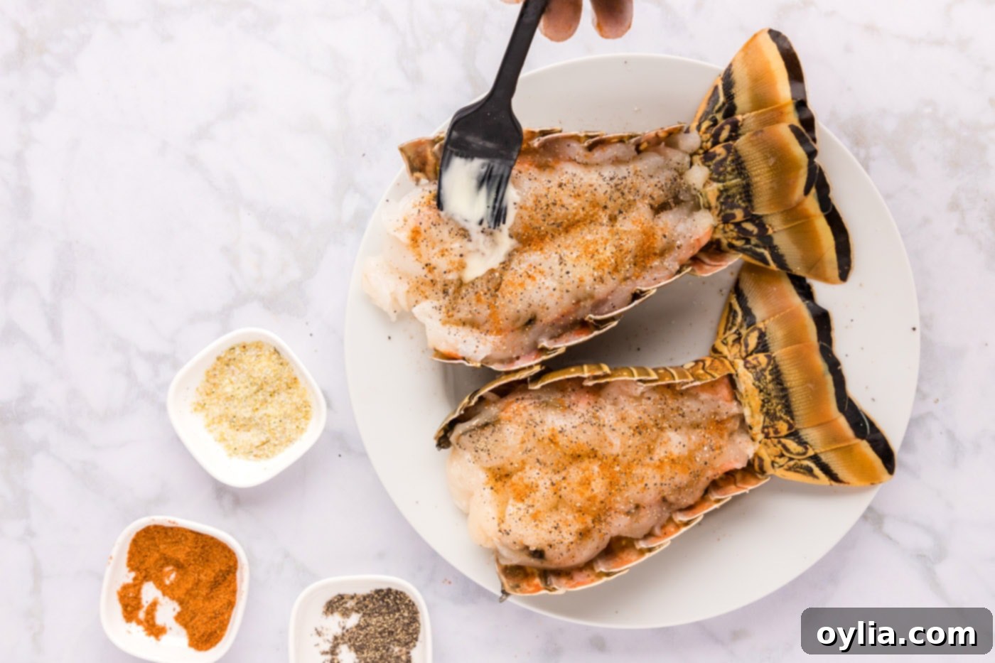 A pastry brush applying softened butter to the seasoned lobster tail meat
