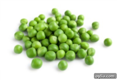 A scattering of fresh young green peas, some still in their pods, on a light surface.
