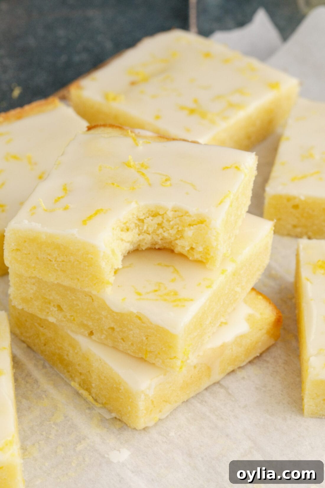 Zesty Lemon Brownies 12 A stack of three Lemon Brownies with a bite taken out of the top one, revealing the moist, golden interior and smooth glaze.