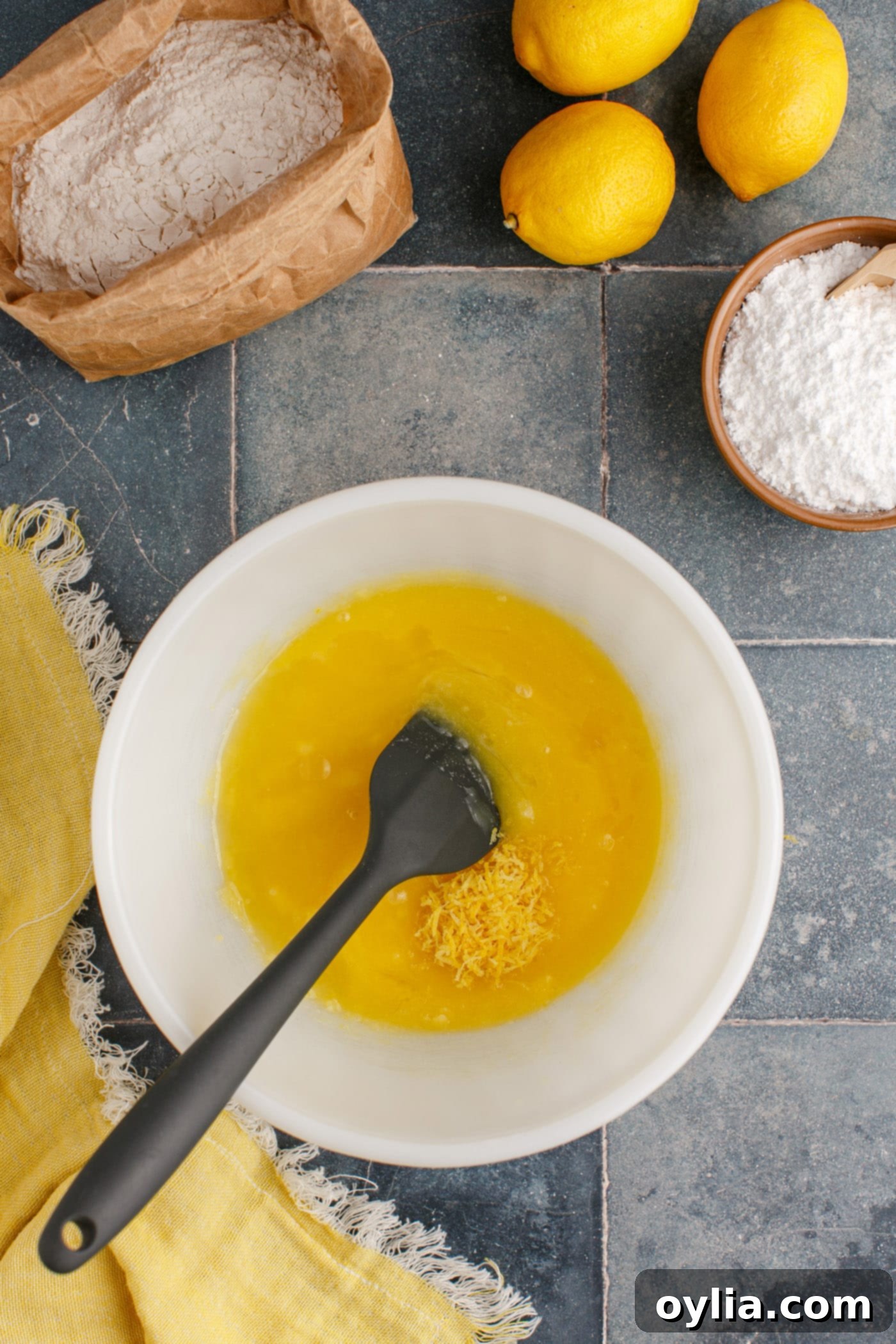 Fresh lemon juice and zest being added to the butter and egg mixture in a bowl, ready to be combined for the brownie batter.