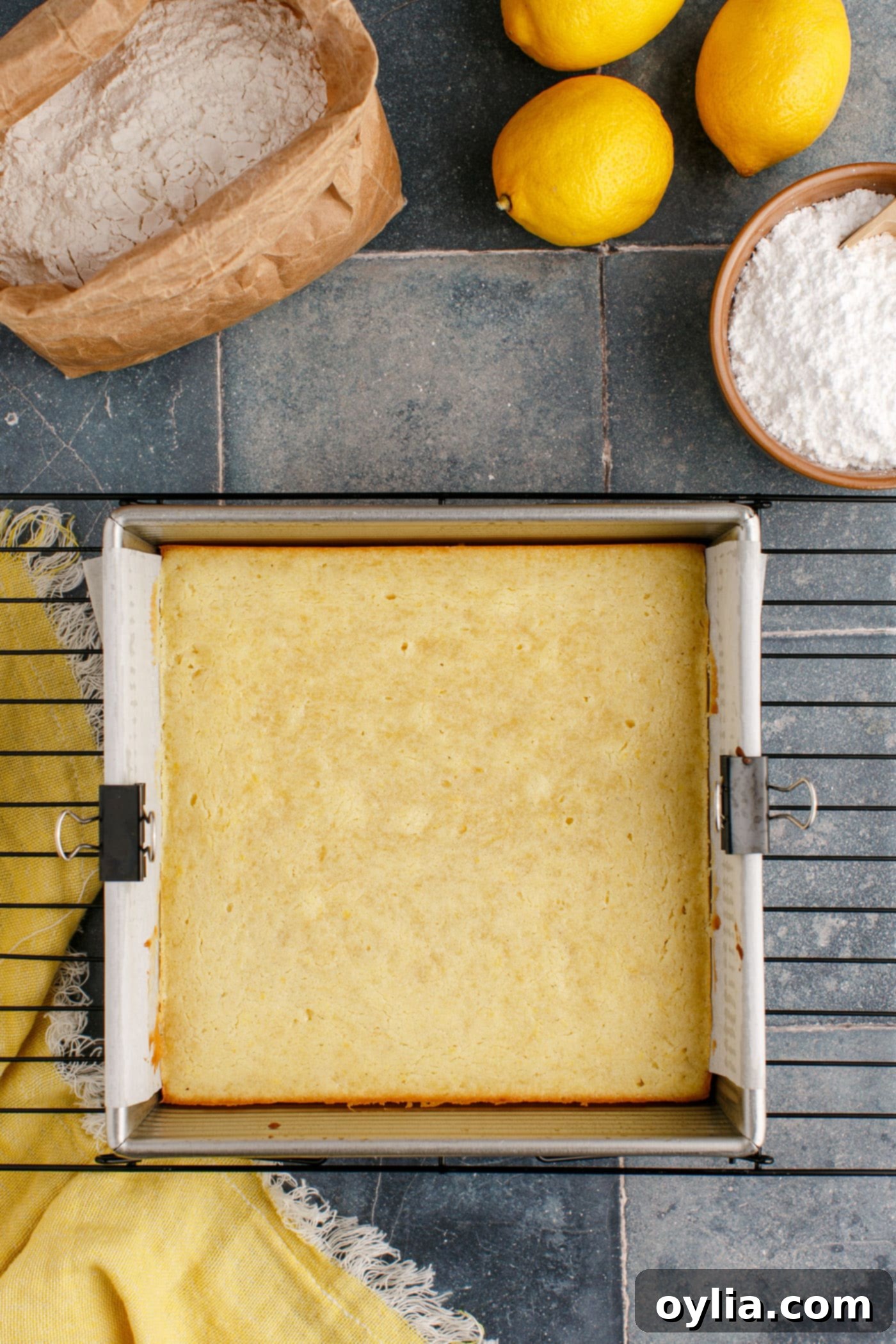 Freshly baked lemon brownies, still in the 8x8 pan, cooling on a wire rack with a golden-brown top.