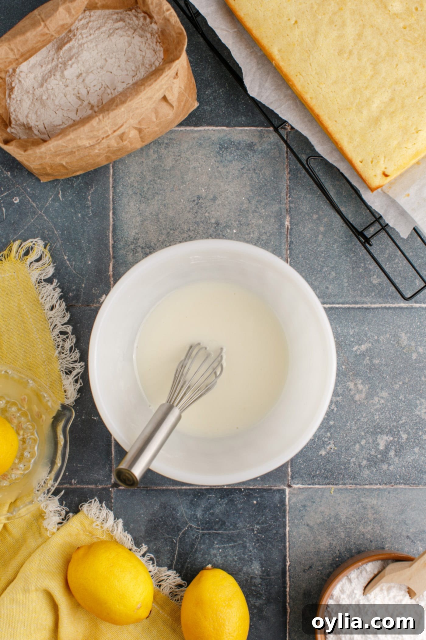 A small mixing bowl holding a smooth, white lemon glaze, with a whisk resting in it.