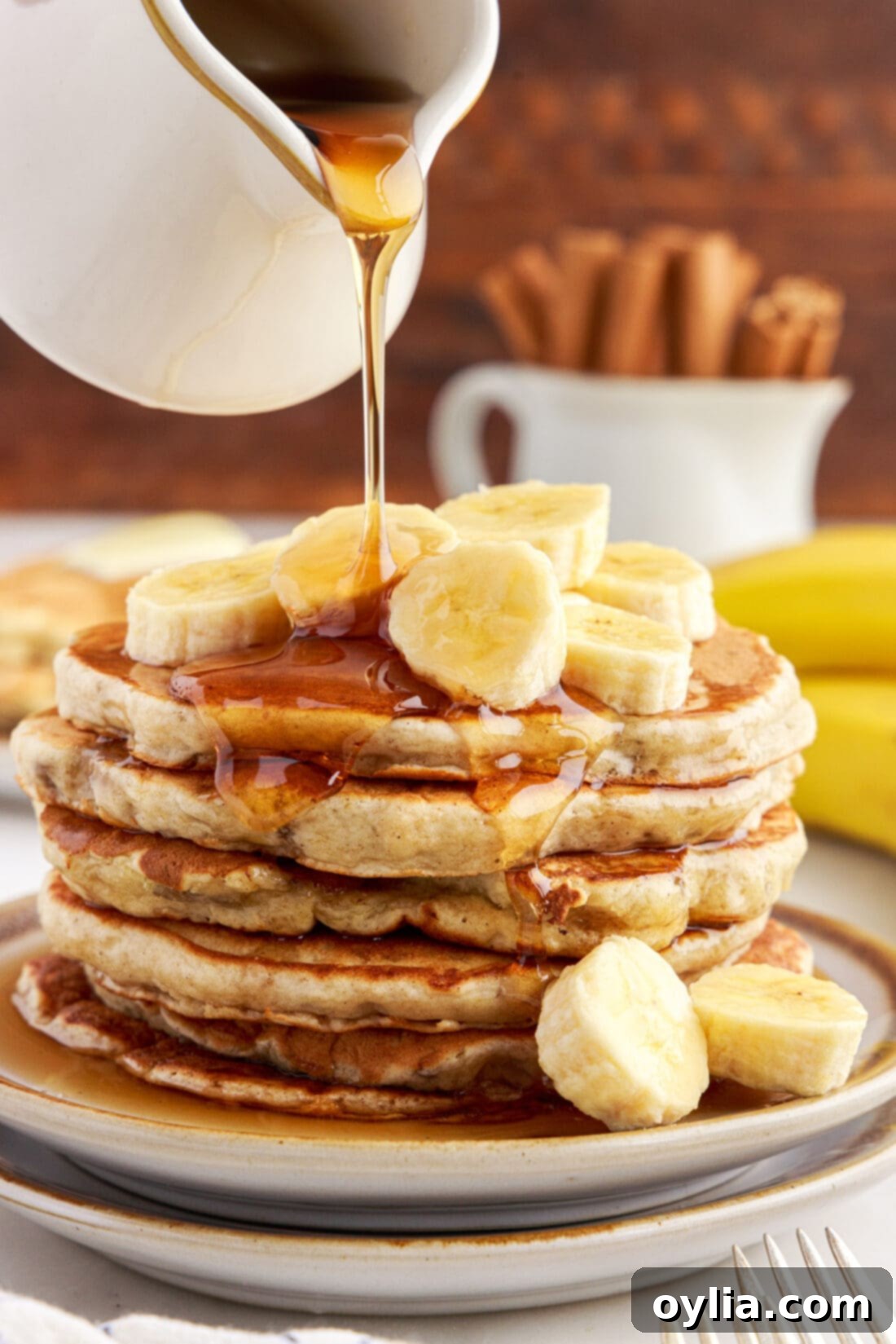 Fluffy Banana Bliss 2 Stack of Fluffy Golden Brown Banana Pancakes with maple syrup being poured on top, ready to be served for breakfast or brunch.