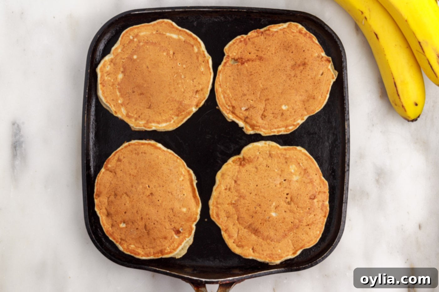 Golden brown banana pancakes cooking on a griddle, showing the perfect doneness on one side.
